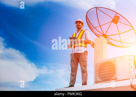 Home lavoratore tuttofare fix refrigeratore di aria e la parabola satellitare stand per il futuro il cielo blu sullo sfondo Foto Stock