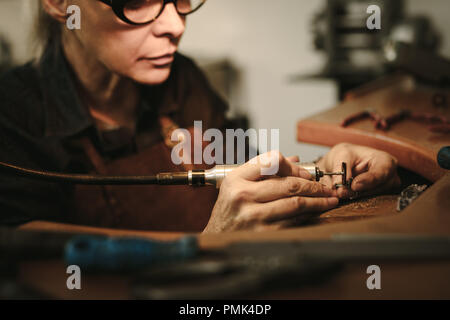 Senior Femminili creatore di gioielli la lucidatura di un prodotto presso il suo banco di lavoro. Designer di Gioielli la lucidatura di un bracciale in officina. Foto Stock