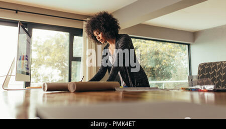 Giovane donna africana lavorando su un piano di costruzione sulla scrivania. Architetto femmina lavora da casa in ufficio. Foto Stock