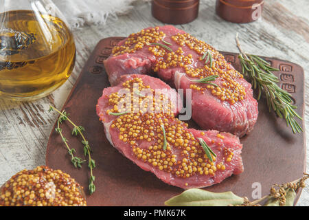 Grigliate di carni bovine pezzi su un tagliere ulivo con marinata di mostarda di Digione, rosmarino e erbe provenzali in uno stile rustico. Foto Stock