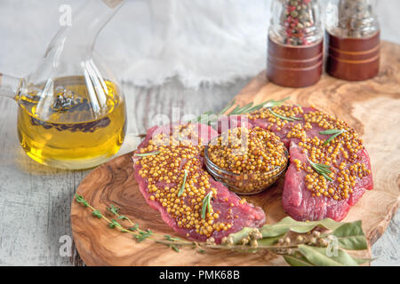 Grigliate di carni bovine pezzi su un tagliere ulivo con marinata di mostarda di Digione, rosmarino e erbe provenzali in uno stile rustico. Foto Stock