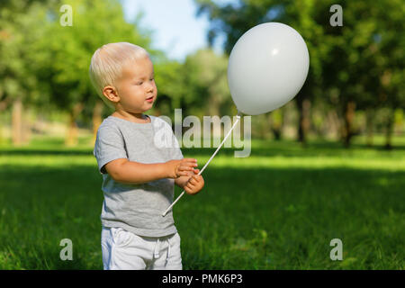 Bambino sorridente tenendo un palloncino bianco in mano Foto Stock
