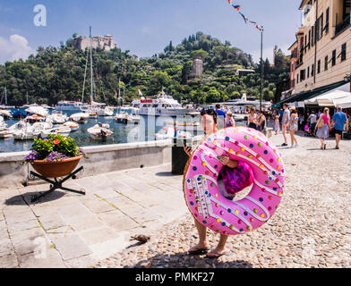 Giovane donna che porta a ciambella gonfiabile a forma di anello, a piedi dal porto, Portofino, Genova, Italia, Europa Foto Stock