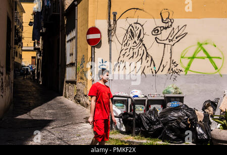 Ragazzo vestito di rosso, camminare passato pila di spazzatura, i graffiti sulla parete in background, Napoli, Italia, Europa Foto Stock