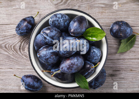 Recipiente di metallo pieno di ripe prune frutta su un tavolo di legno, vista dall'alto Foto Stock
