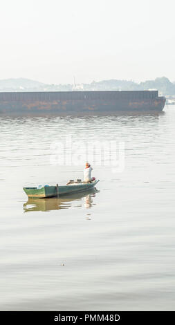 Samarinda / Indonesia - 8/19/2018 : pescatore tradizionale paddling la sua piccola imbarcazione in legno vicino la chiatta passando nel fiume Mahakam Foto Stock