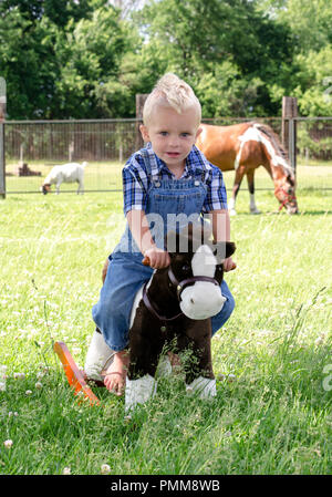 Little Boy su un cavallo a dondolo con cavallo vero dietro Foto Stock