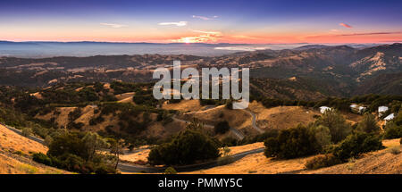 La luce del tramonto illuminano le montagne si trova nella parte sud di San Francisco Bay Area; strada tortuosa discesa attraverso colline; San Jose, California Foto Stock