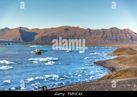 Una laguna riempita di iceberg galleggianti, montagne sullo sfondo azzurro del cielo giorno Foto Stock
