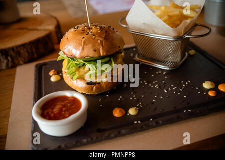Primo piano della hamburger freschi con cesto di patatine fritte sul tavolo di pietra con una ciotola di salsa di pomodoro.gustoso, deliziosi hamburger di manzo con verdure fresche, patatine fritte e coleslaw Foto Stock