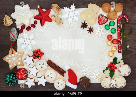 Natale sfondo astratto confine tra cui addobbi per l'albero, i fiocchi di neve, biscotti, torte, spezie e flora invernale su carta pergamena sul rovere rustico Foto Stock