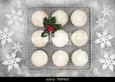 Appena sfornato trito di Natale la torta su un vassoio da forno con lo zucchero a velo e spolvero il simbolo del fiocco di neve ninnolo decorazioni con holly berry rametto di foglia. Vista dall'alto. Foto Stock