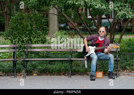 Un uomo in occhiali da sole suonando una chitarra elettrica attraverso un piccolo amplificatore portatile. In Washington Square Park a Manhattan, New York City. Foto Stock