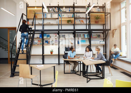 Tre giovani prospettiva startupers seduta nella moderna biblioteca di luce sulla riunione, parlando di nuovo progetto, guardando anche se i dettagli del lavoro, avente giorno produttivo per gli amici atmosfera, Foto Stock