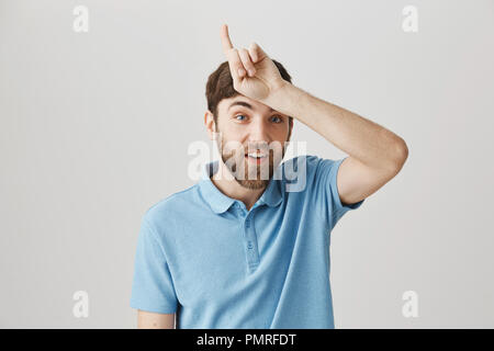 Ho vinto e avete perso. Studio shot di vanteria funny giovane azienda un segno sulla fronte o rivolto verso l'alto con il dito indice, smorfie, in piedi su sfondo grigio. Perdenti devono restare a casa Foto Stock