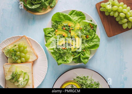 Vegano sana prima colazione. La dieta. Cotta di avocado con uovo e insalata fresca da foglie di rucola, toast e burro. Su un marmo bianco della piastra, un calcestruzzo leggero tabella. Foto Stock