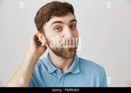 Guy attende mentre la ragazza alla porta si apre. Studio shot di attraenti carino ragazzo europeo con la barba graffiare indietro mentre sorridente largamente e guardando la telecamera, non sapendo come avviare la conversazione Foto Stock