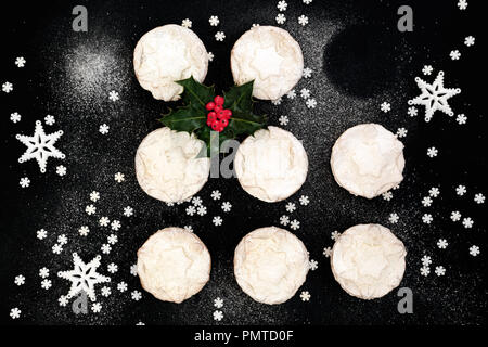 Delizioso pane appena sfornato Natale pasticci di carne macinata con uno mancante, holly berry rametto di foglia, stella decorazioni e zucchero a velo spolvero su sfondo nero. T Foto Stock