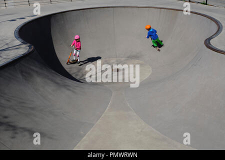 Fratello e Sorella in scooter giocando a sunny skate park Foto Stock