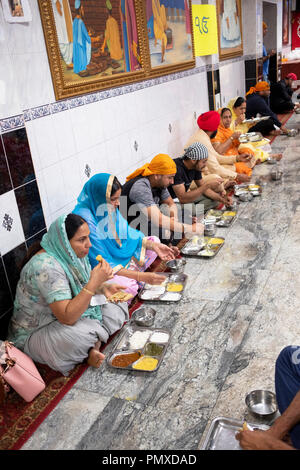 Donne e uomini di mangiare in un tempio sikh langar dove gratuitamente un pasto vegetariano è servita a chiunque senza eccezione. In Richmond Hill, Queens, a New York. Foto Stock