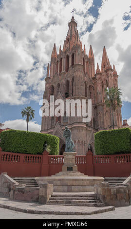 Bella Parroquia de San Miguel Arcángel, con la statua di Fray Juan de San Miguel in primo piano verde e drammatica nuvoloso cielo blu Foto Stock