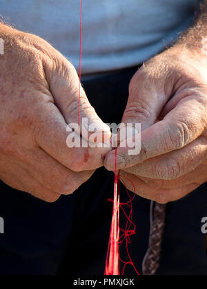 Le mani del pescatore riparando il suo rosso rete da pesca , close up dettaglio Foto Stock