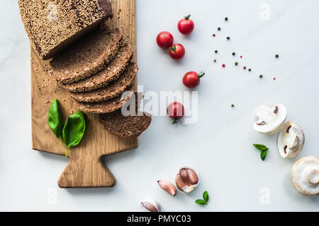 Lay piatto con fette di pane sul tagliere di legno, pepe nero e ortaggi per cucinare la colazione su marmo bianco superficie Foto Stock