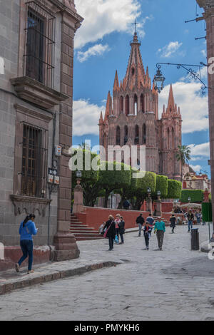 San Miguel De Allende, Mexico-October 26, 2017: Parroquia de San Miguel Arcangel, che domina il El Jardin, un nuvoloso cielo blu, e gente che cammina Foto Stock