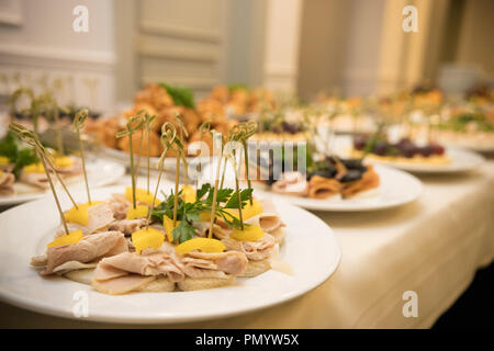 Fila di lastre con vari antipasti freddi in piedi su un tavolo con una tovaglia bianca Foto Stock