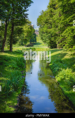 Bella con flusso di erba verde e alberi e la Belweder Palace all'orizzonte nel Parco Lazienki a Varsavia in Polonia. Foto Stock