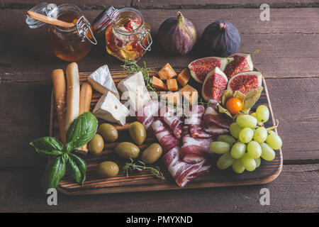 Figg,formaggio camembert,prosciutto ,olive e uva sul buio che serve scheda sopra rustico sfondo di legno Foto Stock