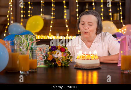 Donna anziana festeggia il suo compleanno a casa. Senior donna soffiando candele sulla torta di compleanno. Celebrando il concetto di invecchiamento. Foto Stock