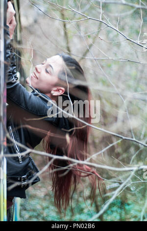 Bruna giovane donna appendere fuori di un treno abbandonato finestra nel bosco con lunghi capelli rossi Foto Stock