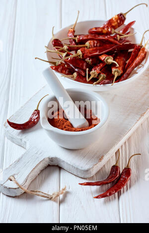 Vista ravvicinata del Peperoncino macinato il pepe in un mortaio con pestello bianco su una superficie di legno Foto Stock