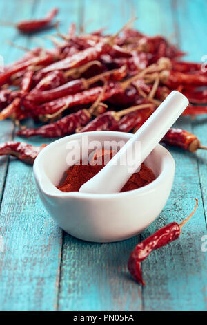 Vista ravvicinata del Peperoncino macinato il pepe in un mortaio con pestello su blu superficie in legno Foto Stock