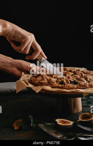 Ritagliato colpo di donna torta di taglio sulla carta da forno con il coltello sul piano portapaziente con figure Foto Stock