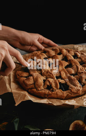 Ritagliato colpo di donna torta di taglio sulla carta da forno con il coltello Foto Stock