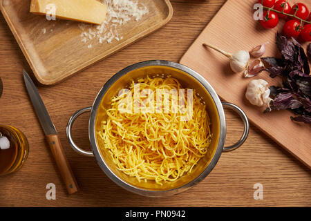 Cuocere gli spaghetti in metallo scolapasta circondato con gli ingredienti per la pasta sul tavolo di legno Foto Stock