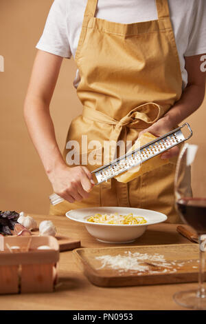 Ritagliato colpo di donna grattugiare il formaggio durante la cottura della pasta Foto Stock