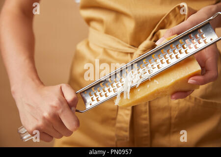 Ritagliato colpo di donna in grembiule yellop grattugiare il formaggio Foto Stock