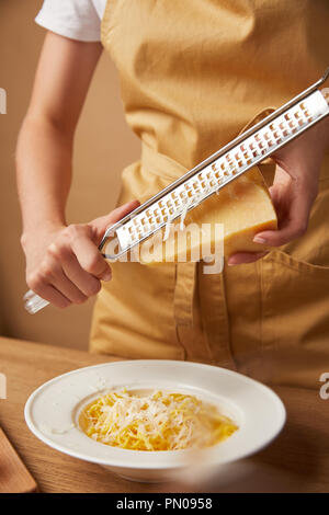 Ritagliato colpo di donna grattugiare il formaggio su spaghetti Foto Stock