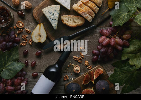 Vista superiore della bottiglia di vino con etichetta vuota, frutta fresca e deliziosi spuntini sul tavolo di legno Foto Stock