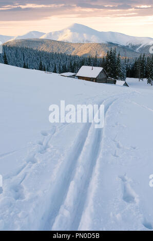 Montagne innevate in inverno. La dolce luce del sole al tramonto. Vista di un villaggio con case in legno. Sciare in neve fresca dopo la nevicata Foto Stock