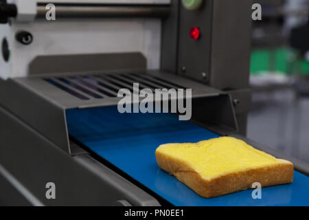 Il burro spalmato sul pane fresco fetta nella linea di produzione sul nastro trasportatore automatico di pancarrè imburrandolo macchina in fabbrica da forno. per alimenti industriali con Foto Stock