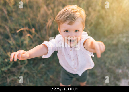 Angolo di alta vista adorabile ragazzino raggiungendo le mani e sorridendo a videocamera all'esterno Foto Stock