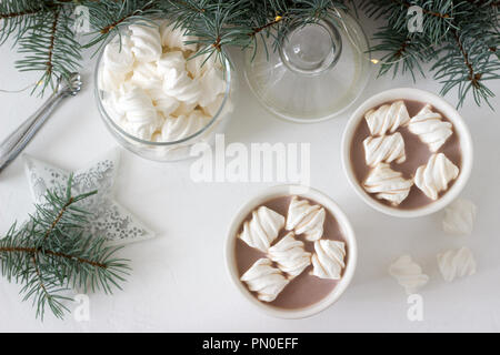 Il cacao con marshmelow in bianco tazze e marshmallows in un vasetto di vetro su un tavolo bianco con rami di abete rosso, una ghirlanda di fiori e una stella bianca. Messa a fuoco selettiva Foto Stock