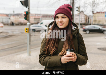 Una ragazza beve caffè da una tazza monouso in strada a Praga nel tempo fresco. La solita vita quotidiana. Foto Stock