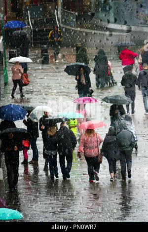 Guardando attraverso un raindrop finestra coperto a persone fuori shopping e catturati in autunno pesante con doccia a pioggia. Foto Stock