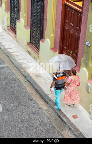 Coppia cubana camminare sotto ombrello sotto la pioggia, Havana, Cuba Foto Stock