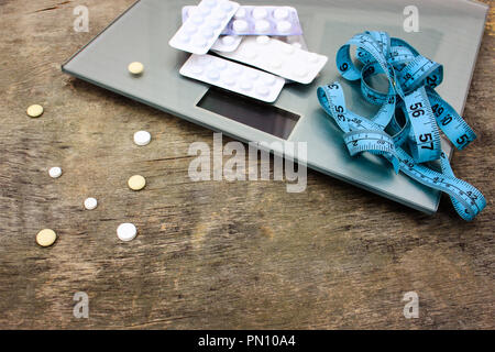Nastro di misurazione, pillole e scale su sfondo di legno. Il concetto delle pillole di dieta. Foto Stock